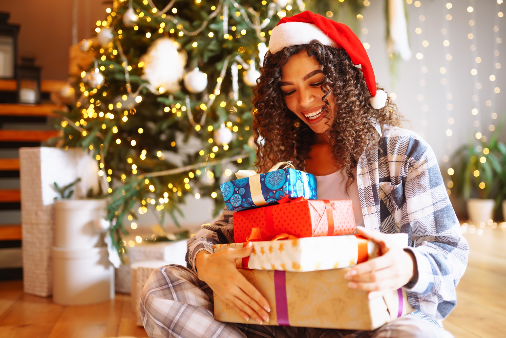Young woman with Christmas gifts at home near Christmas tree. Winter holidays. New Years.